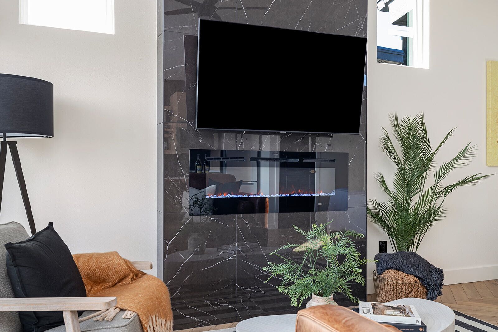 Una sala de estar moderna con un televisor de pantalla plana montado en una pared de mármol, una lámpara de pie, un sofá con cojines, una mesa de centro y una planta en maceta.