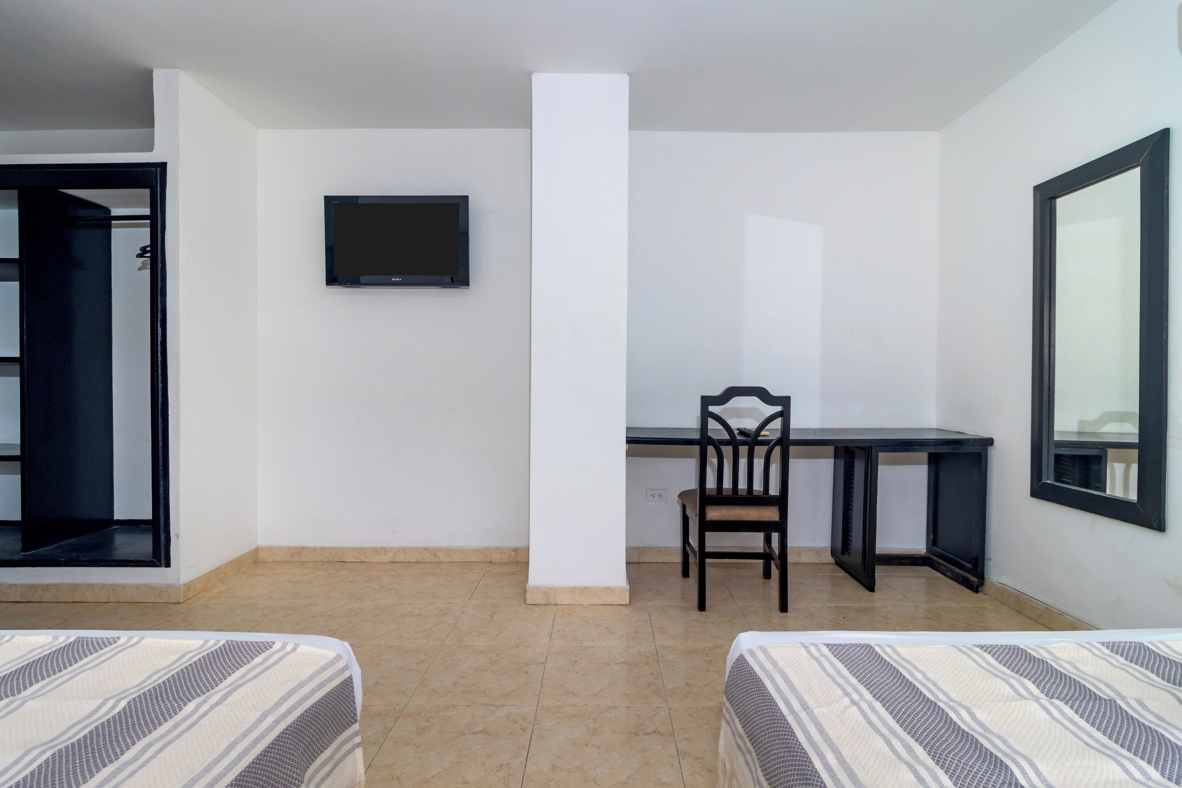 Quarto de hotel com cama, escrivaninha, cadeira, televisão e janela.