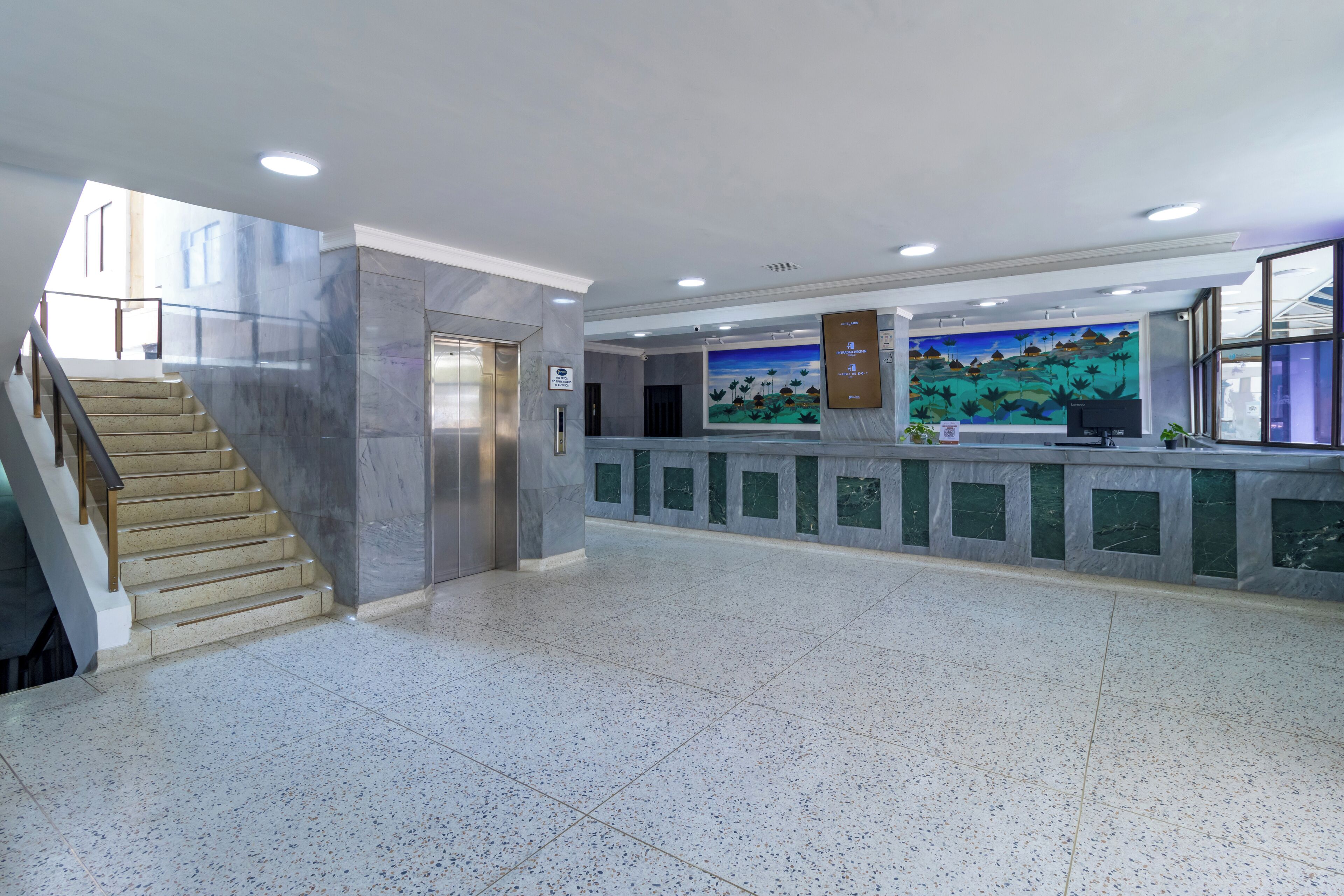 Un vestíbulo espacioso con una escalera de mármol, una recepción y un mural en la pared.