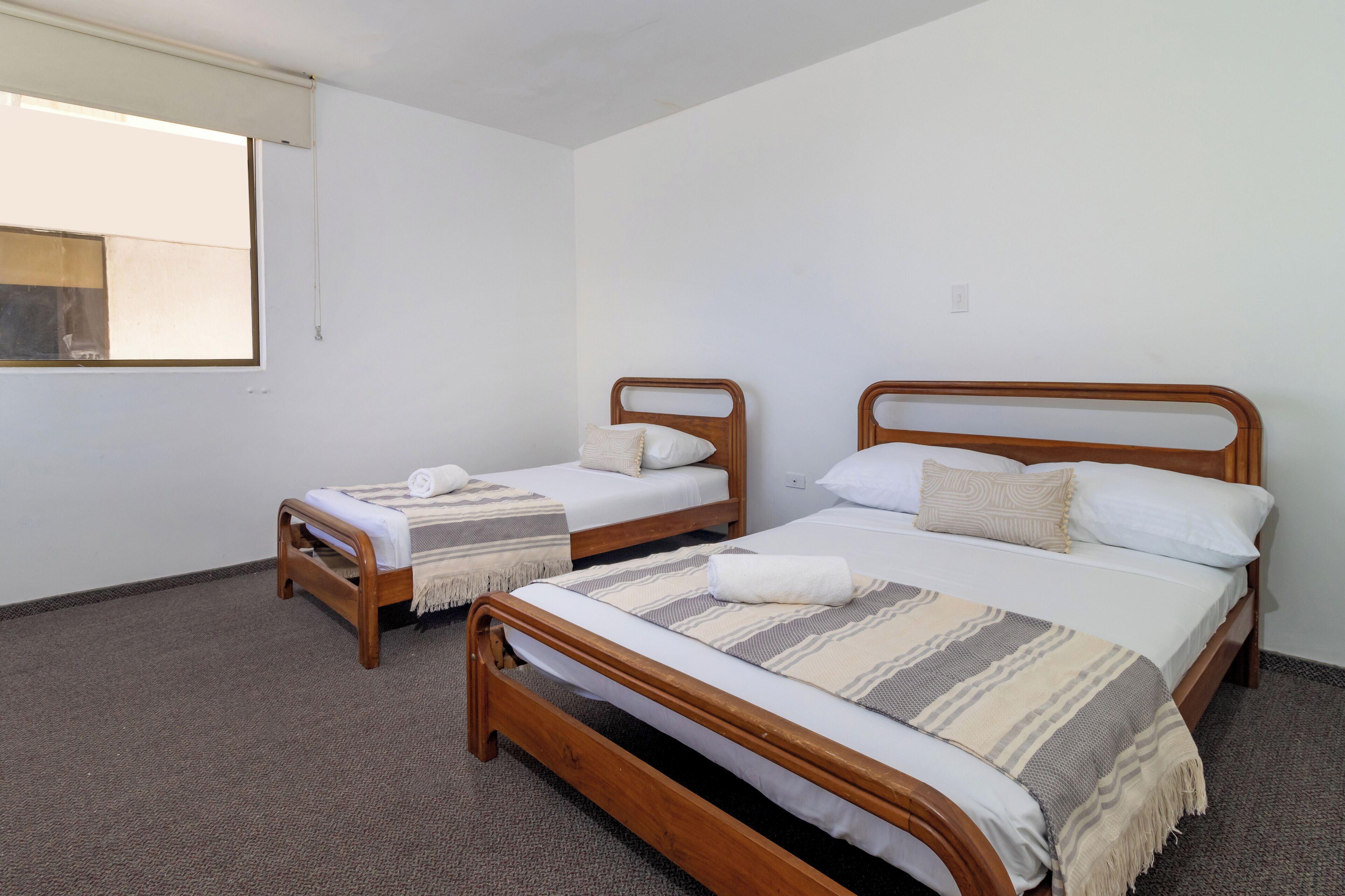 A room with two wooden beds, each with white linens and a blanket.