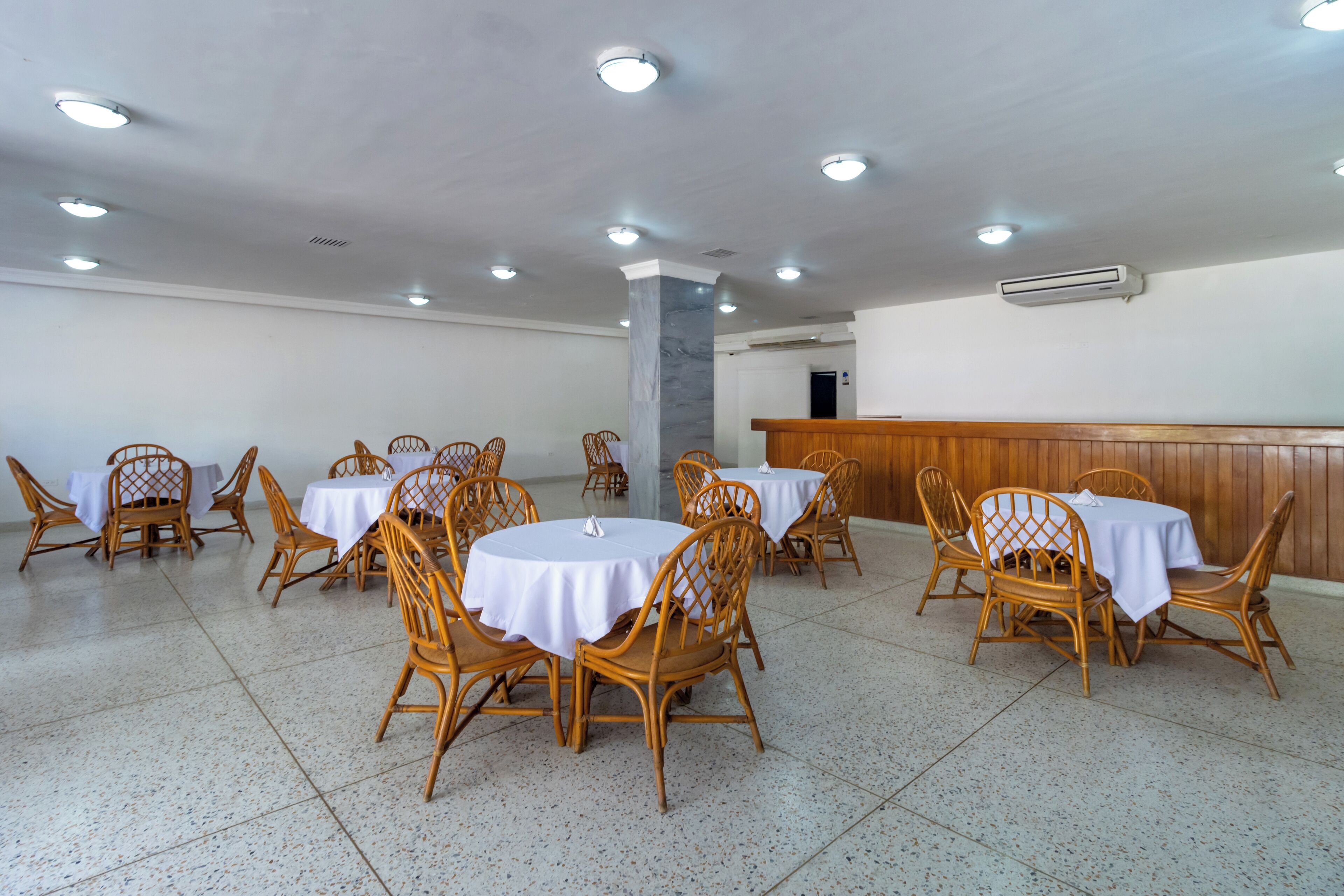 A spacious dining area with round tables and wicker chairs, a marble pillar, and a wooden counter.