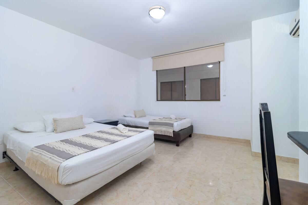 A bedroom with two beds, a TV, and a window with blinds.
