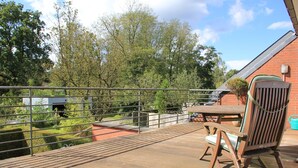A wooden deck with a metal railing, a brick wall, and a table with chairs. - Maison Spacieuse near Brussels (Meise)