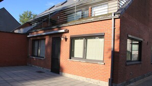 A red brick building with a tiled patio, large windows, and a metal balcony. - Maison Spacieuse near Brussels (Meise)
