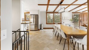 A modern kitchen with a large island, stainless steel appliances, and a dining area with a long wooden table and white chairs.