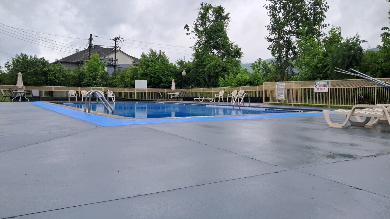 Piscina exterior con cubierta azul, rodeada de una cerca y árboles.