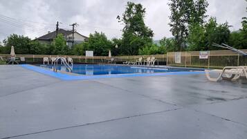 Una piscina exterior amb una zona blava, envoltada per una tanca i arbres.