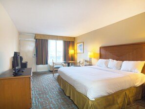 Een hotelkamer met een groot bed, een bureau met een computer, een stoel, een tafel en een raam met gordijnen.
