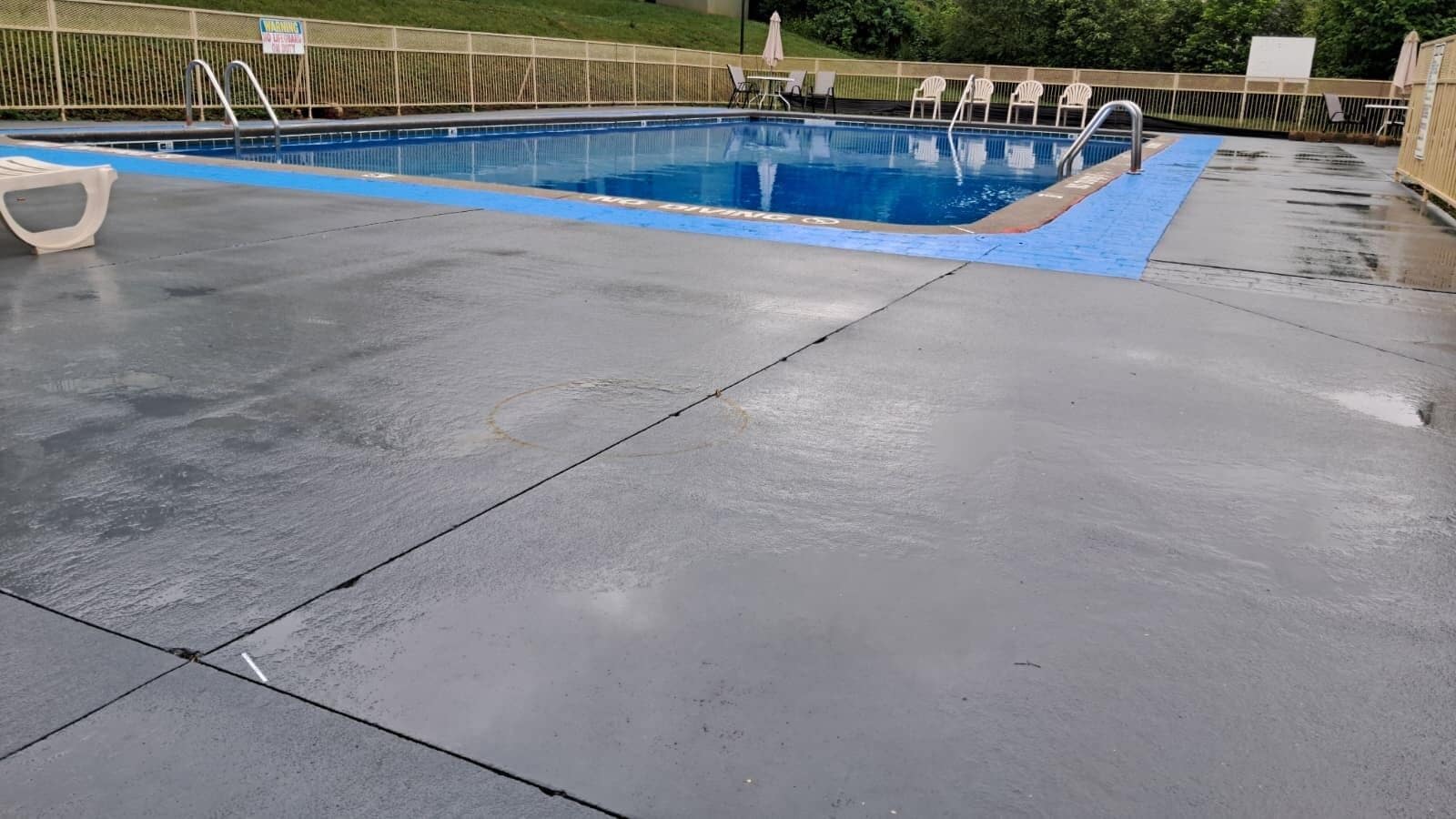 Una piscina con borde azul, rodeada por una valla y sillas.