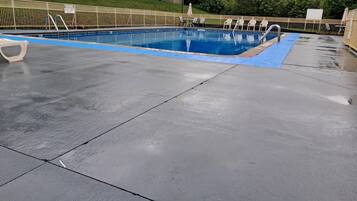 Una piscina con borde azul, rodeada por una valla y sillas.