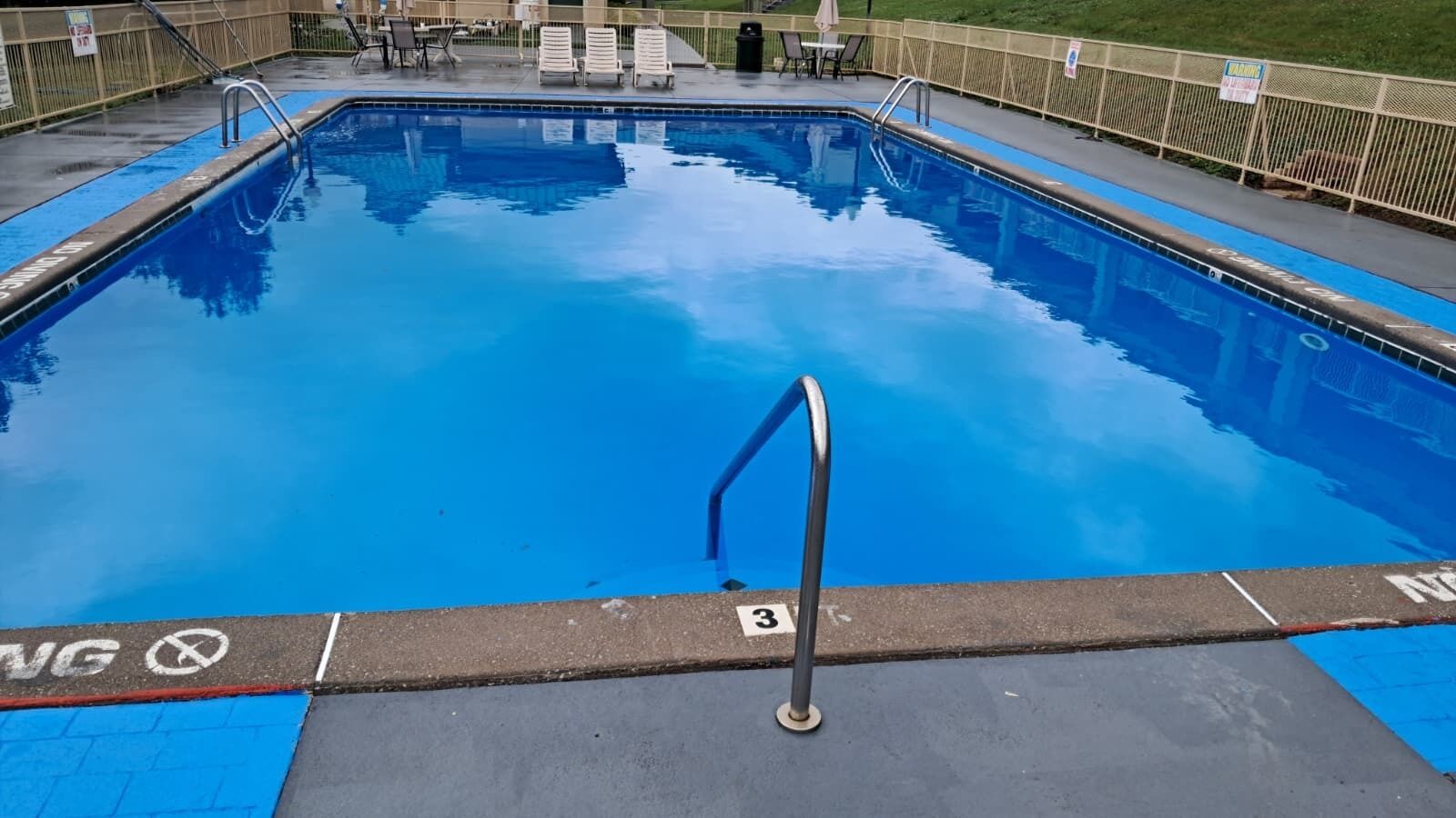Una piscina rectangular con revestimiento azul, una escalera metálica y un letrero con el número 3 en el borde.
