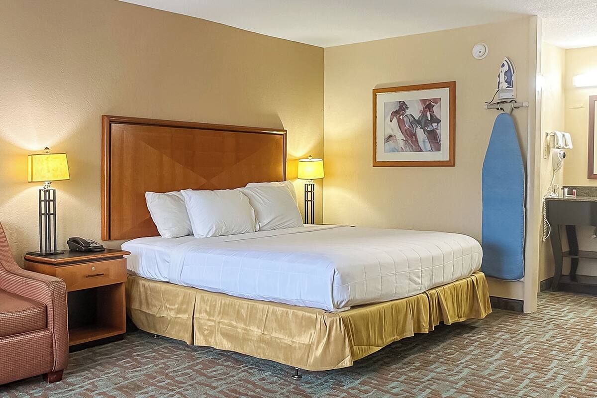 Ein Hotelzimmer mit einem großen Bett, zwei Nachttischlampen, einem Sessel, einem Schreibtisch und einem Spiegel.