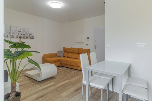 A modern living room with a white sofa, a dining table with chairs, a large plant, and a painting on the wall. - Carmo Palace I (Funchal)