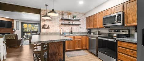 A modern kitchen with wooden cabinets, a central island, stainless steel appliances, and a brick accent wall.