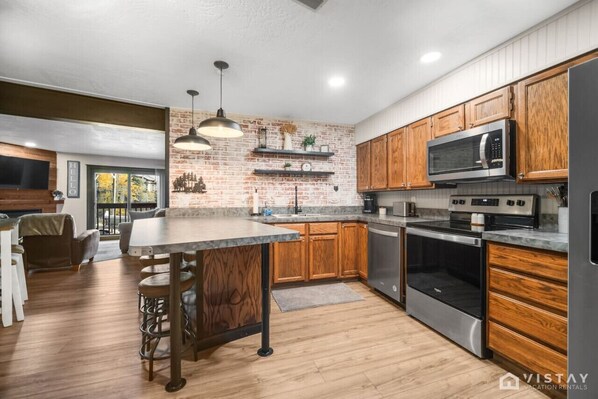 Una cocina moderna con armarios de madera, una isla central, electrodomésticos de acero inoxidable y una pared de ladrillo decorativa.