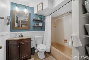 Un baño con tocador de madera, inodoro blanco, bañera y cortina de ducha.