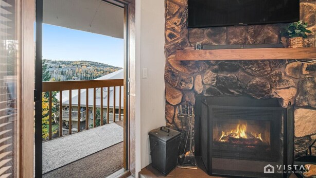 Una chimenea de piedra con un televisor encima, un balcón con barandilla y vistas a un pueblo.