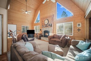A spacious living room with a fireplace, wooden walls, and large windows.