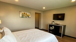 A hotel room with a bed, bedside table, lamp, phone, TV, and a painting on the wall. - Four Seasons Inn (Gallipolis)