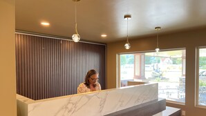 A reception desk with a marble top, wooden paneling on the wall, and pendant lighting. - Four Seasons Inn (Gallipolis)
