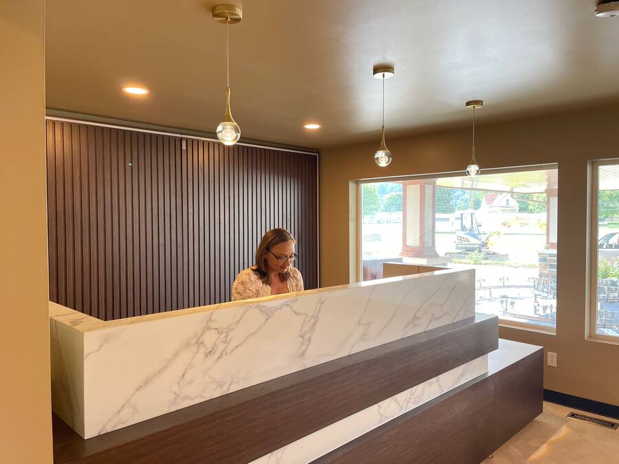 A reception desk with a marble top, wooden paneling on the wall, and pendant lighting.