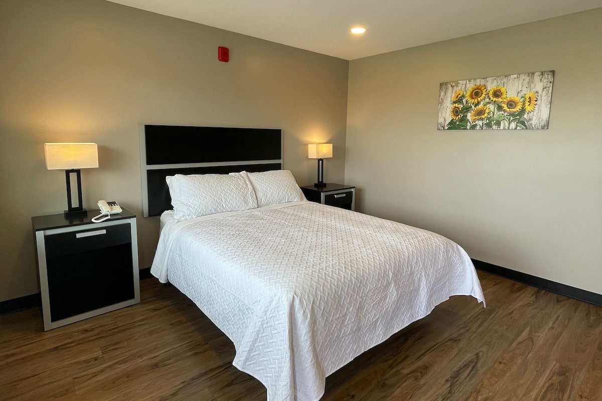 A hotel room with a bed, two bedside tables with lamps, a painting of sunflowers, and a ceiling light.