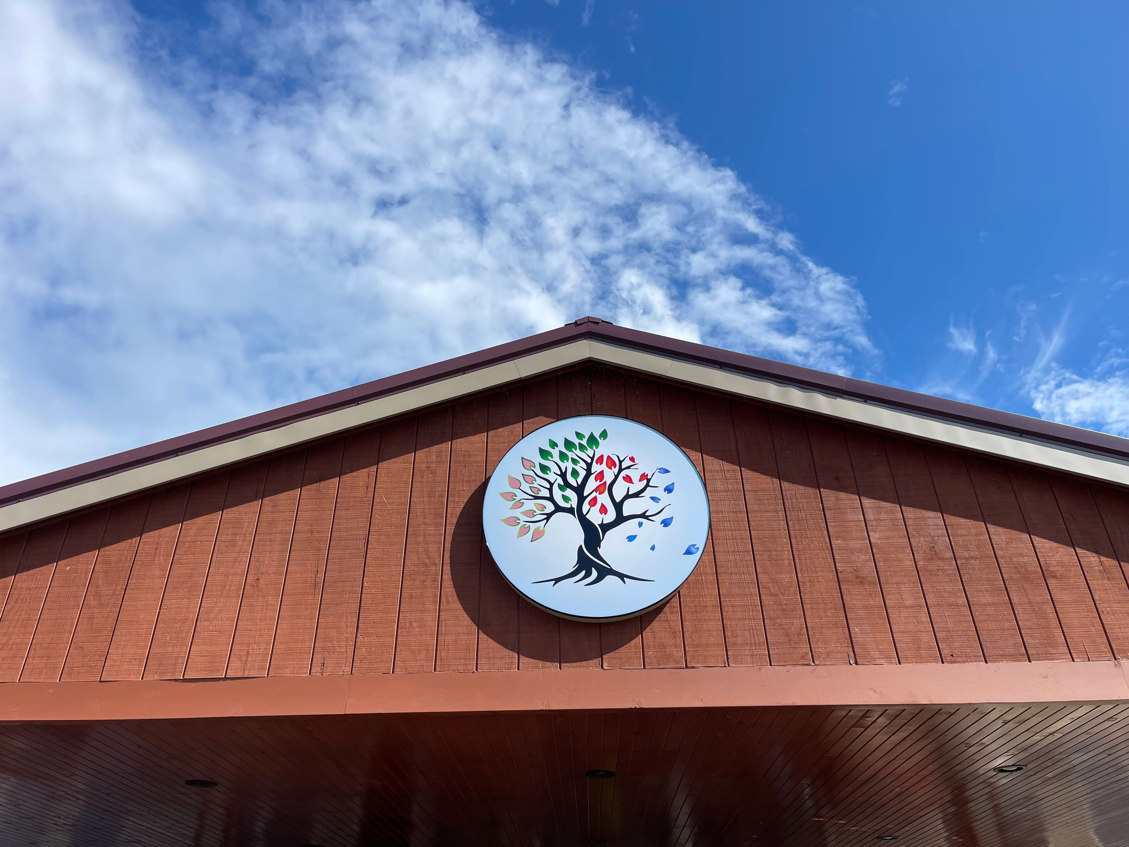 Un edificio con fachada de madera y un logo circular que muestra un árbol con hojas de colores.