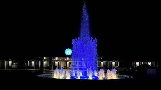 A nighttime view of a hotel with a central fountain, illuminated by blue lights, and a circular logo above the entrance. - Four Seasons Inn (Gallipolis)