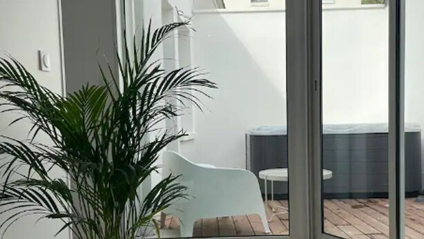 Een modern interieur met een potplant, een witte stoel en een glazen schuifdeur naar een buitenruimte met een tafel en een stoel.