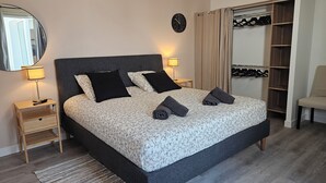 Een keurig opgemaakt slaapkamer met een bed, nachtlampjes, een spiegel, een klok, een garderobe en een stoel.