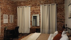 Un dormitorio con pared de ladrillo, una cama con ropa de cama blanca y marrón, un ventilador de techo y un espejo en la pared.