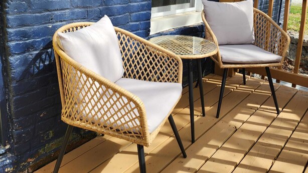 Una terraza de madera con sillas de mimbre y una pequeña mesa de vidrio.