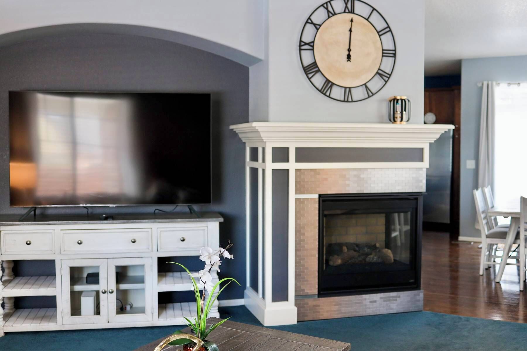 Ein Wohnzimmer mit einem großen Flachbildfernseher, einem Kamin und einer Wanduhr.