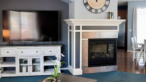 A living room with a large flat-screen TV, a fireplace, and a clock on the wall. - Immaculate Home in Aurora (Aurora)