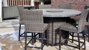 An outdoor patio with a round table and wicker chairs, a brick wall, and a grill. - Immaculate Home in Aurora (Aurora)
