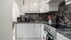 Une cuisine avec des meubles blancs, un plan de travail noir, une cuisinière et un four à micro-ondes.