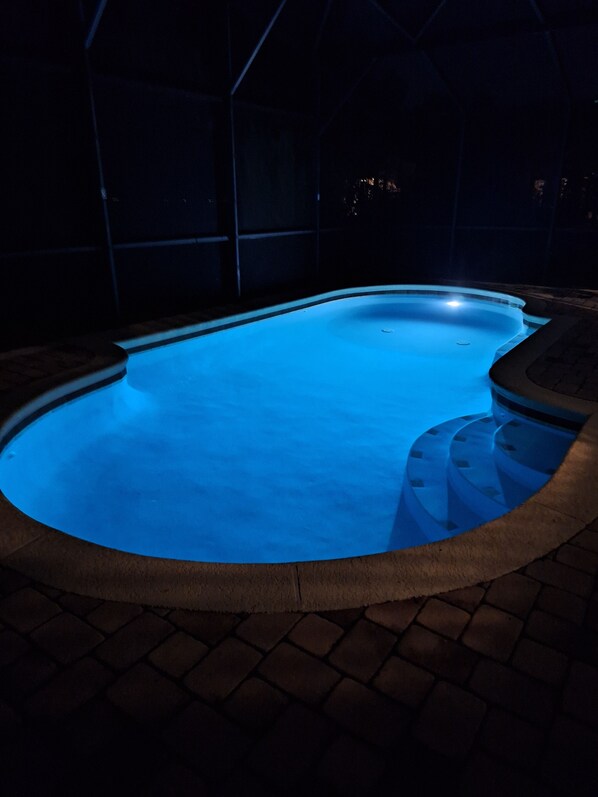 A swimming pool with a blue-lit edge, surrounded by a stone deck.