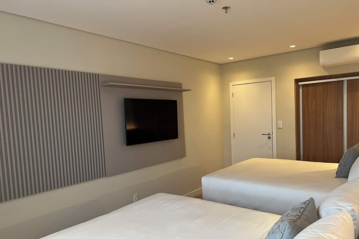 Quarto de hotel com duas camas, uma televisão de tela plana na parede e um guarda-roupa.