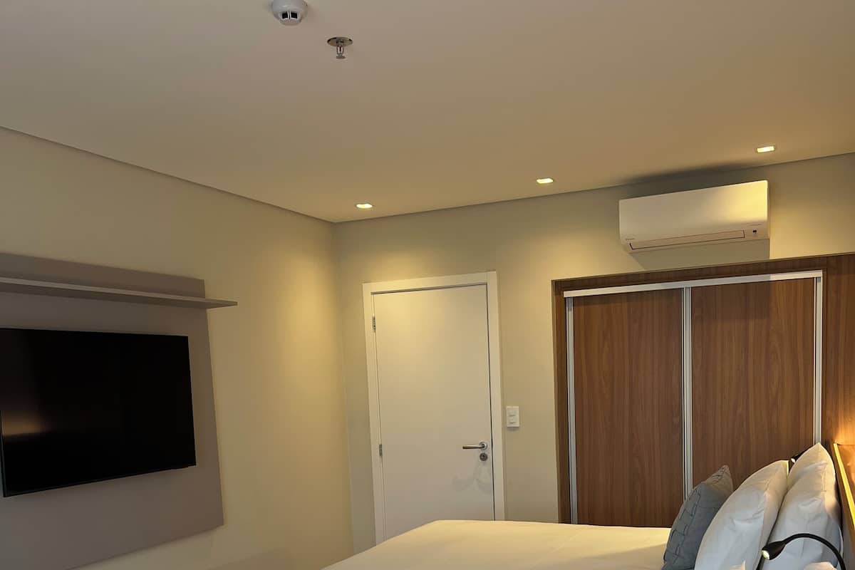 Quarto de hotel com duas camas de solteiro, televisão na parede, guarda-roupa e ar condicionado.