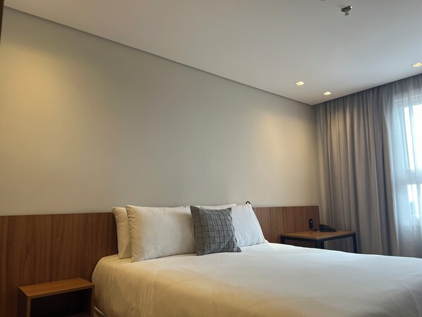 Camera d'albergo con un letto grande, una testiera in legno, due comodini e una finestra con tende.