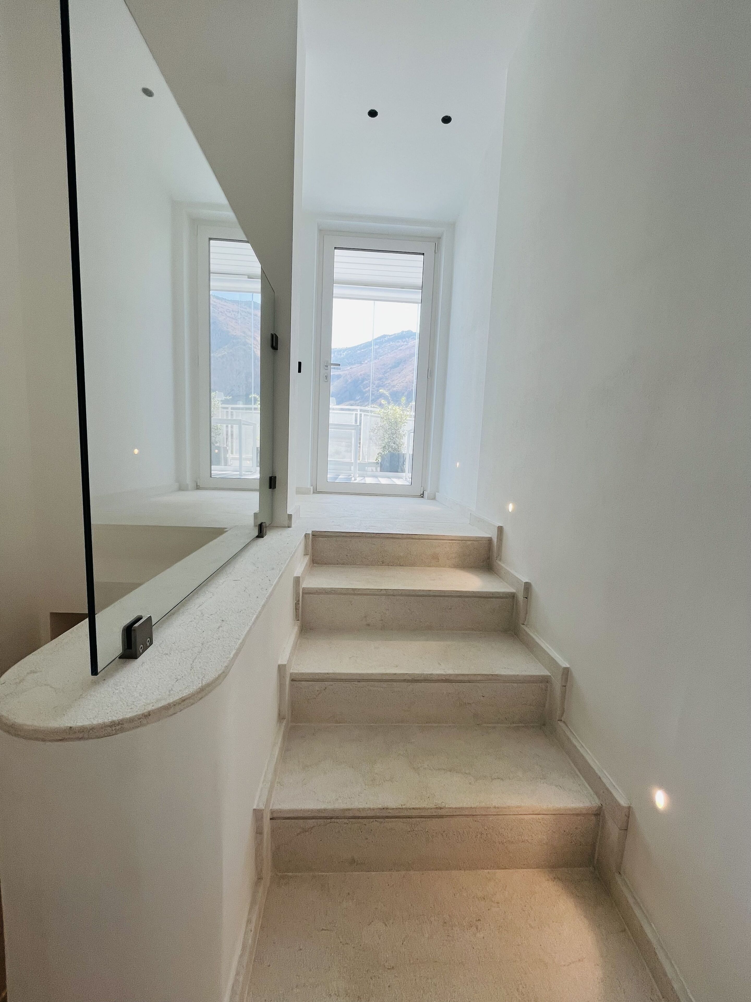 A staircase with a handrail, leading to a door with a view of mountains.