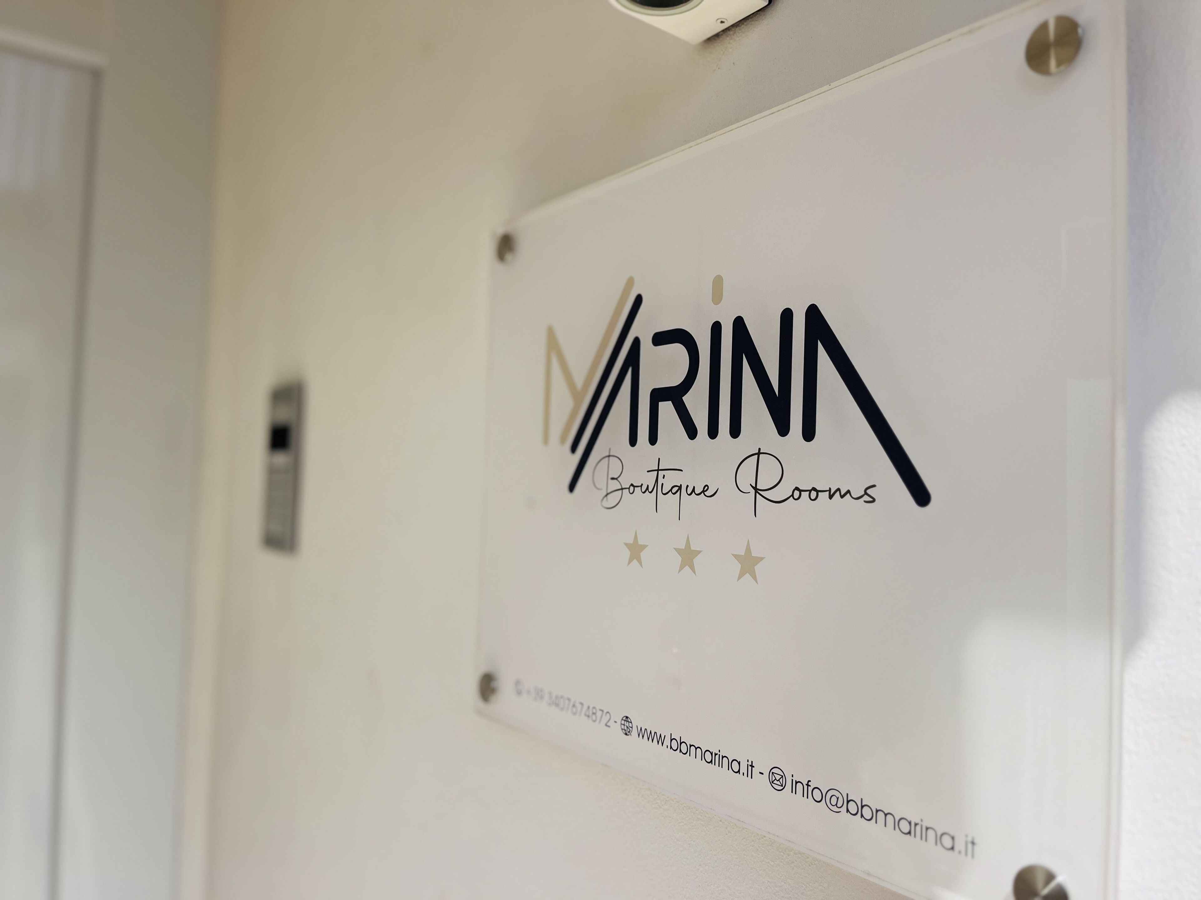 A sign for 'MARINA Boutique Rooms' with contact information and a website URL.