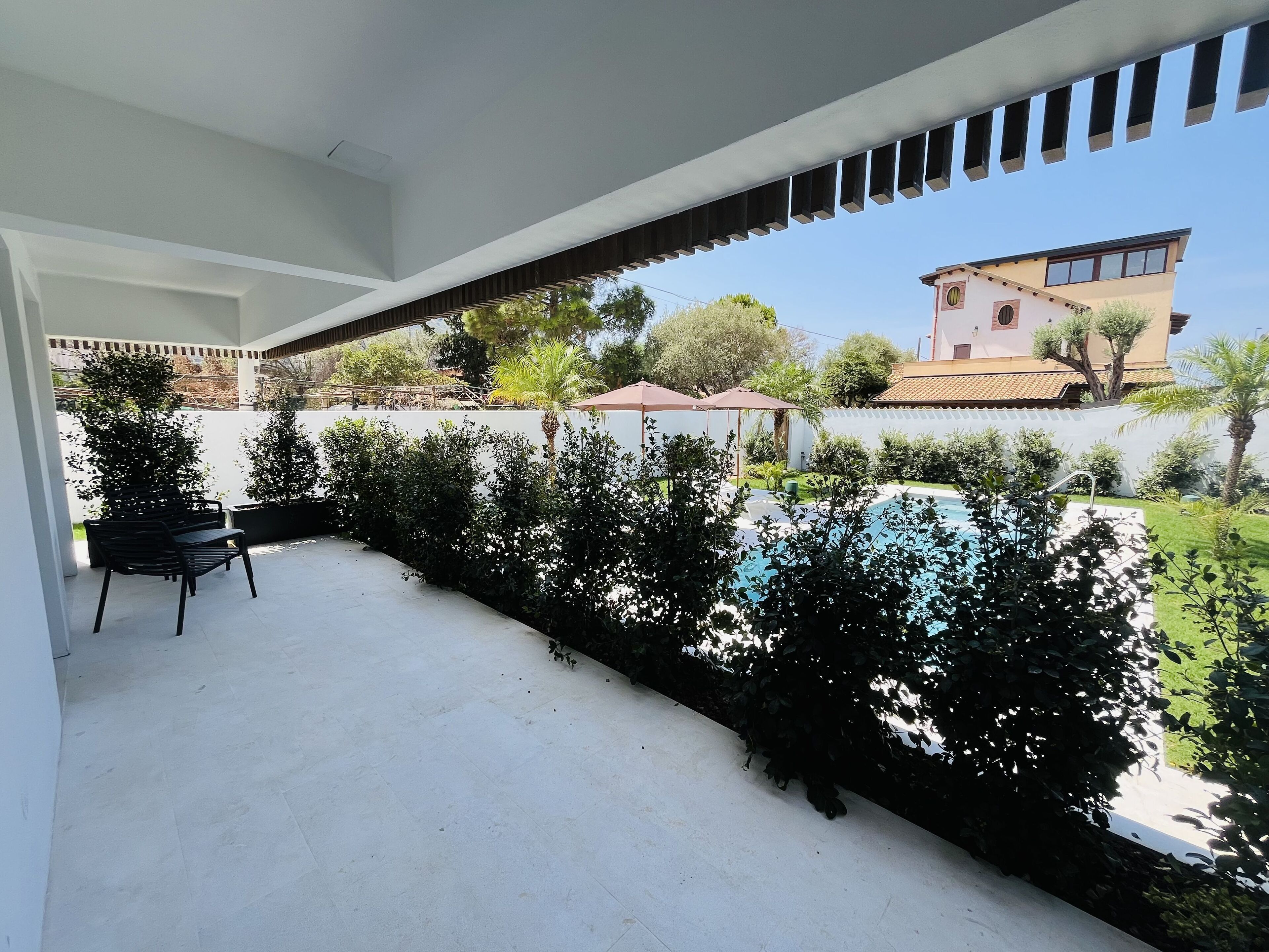 Un espacio al aire libre techado con piscina, un patio con sillas y vista a un edificio en el fondo.
