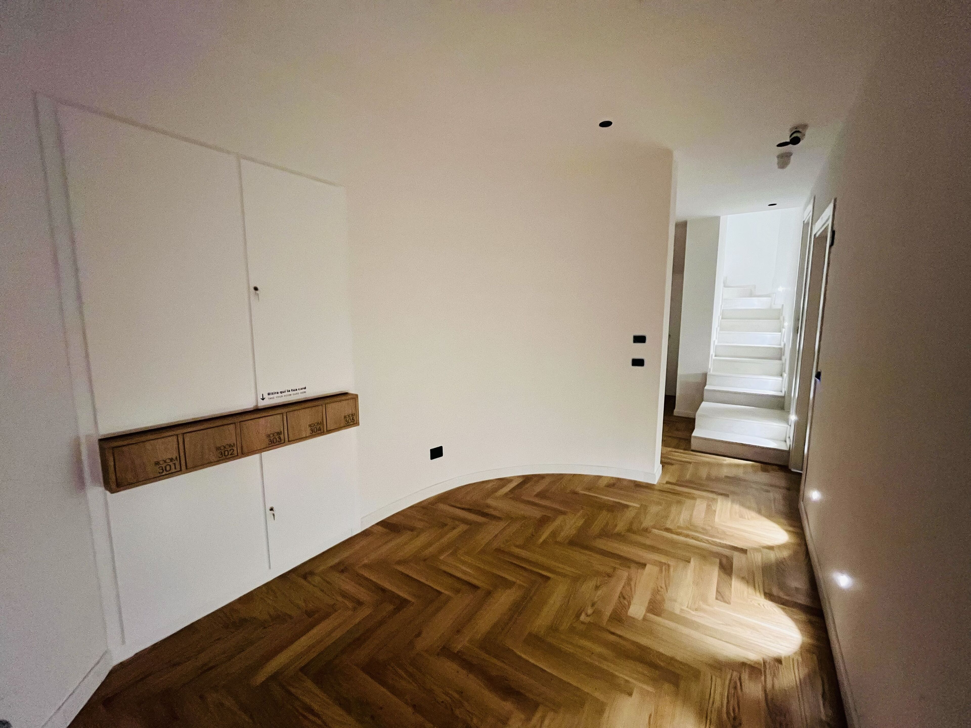 A hallway with wooden flooring, white walls, and a staircase leading to another level.