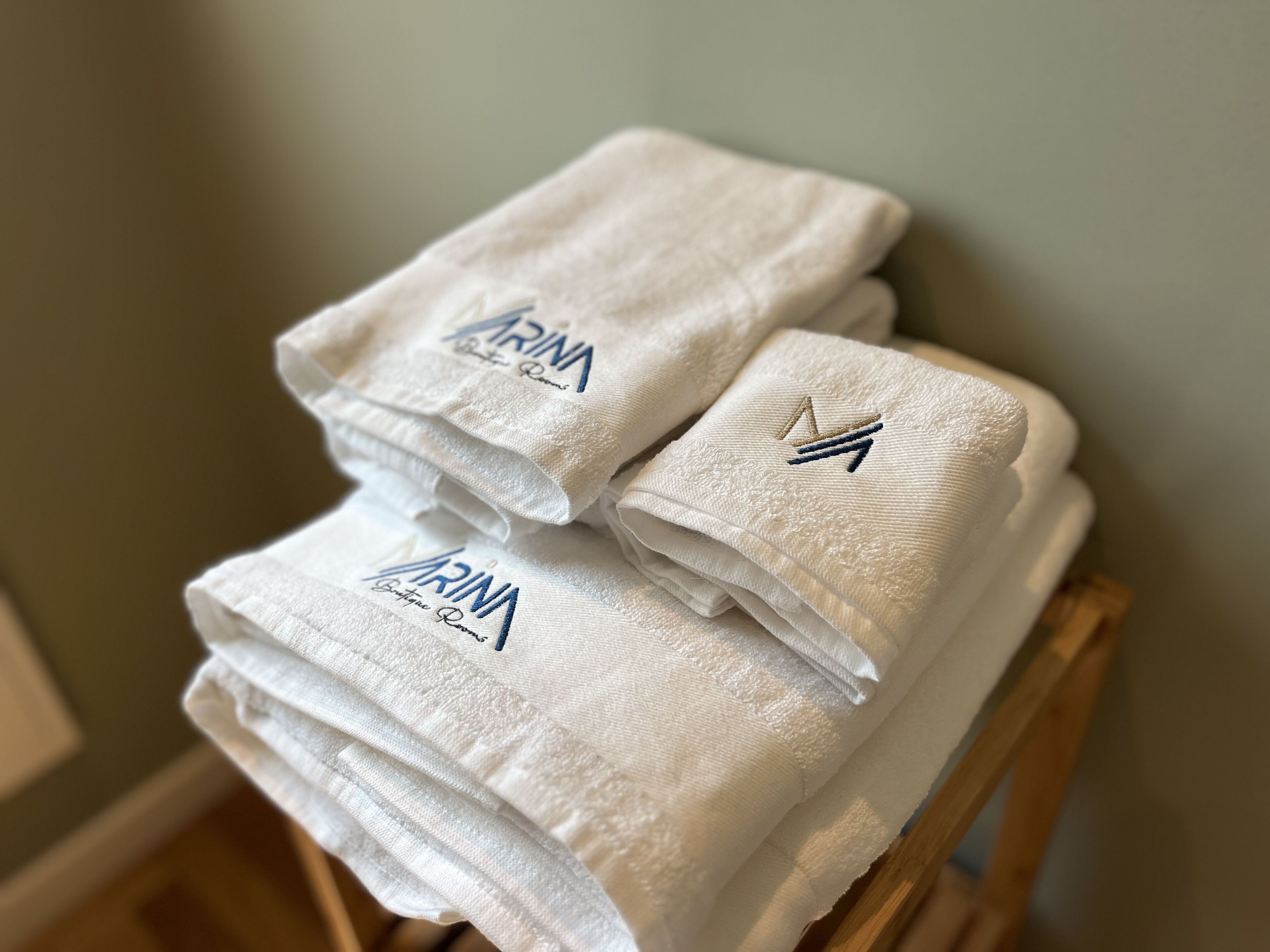 Uma pilha de toalhas brancas com texto bordado e um logotipo sobre uma cadeira de madeira.