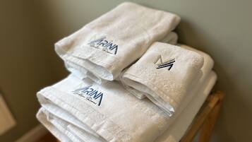 Una pila de toallas blancas con texto bordado y un logotipo sobre una silla de madera.