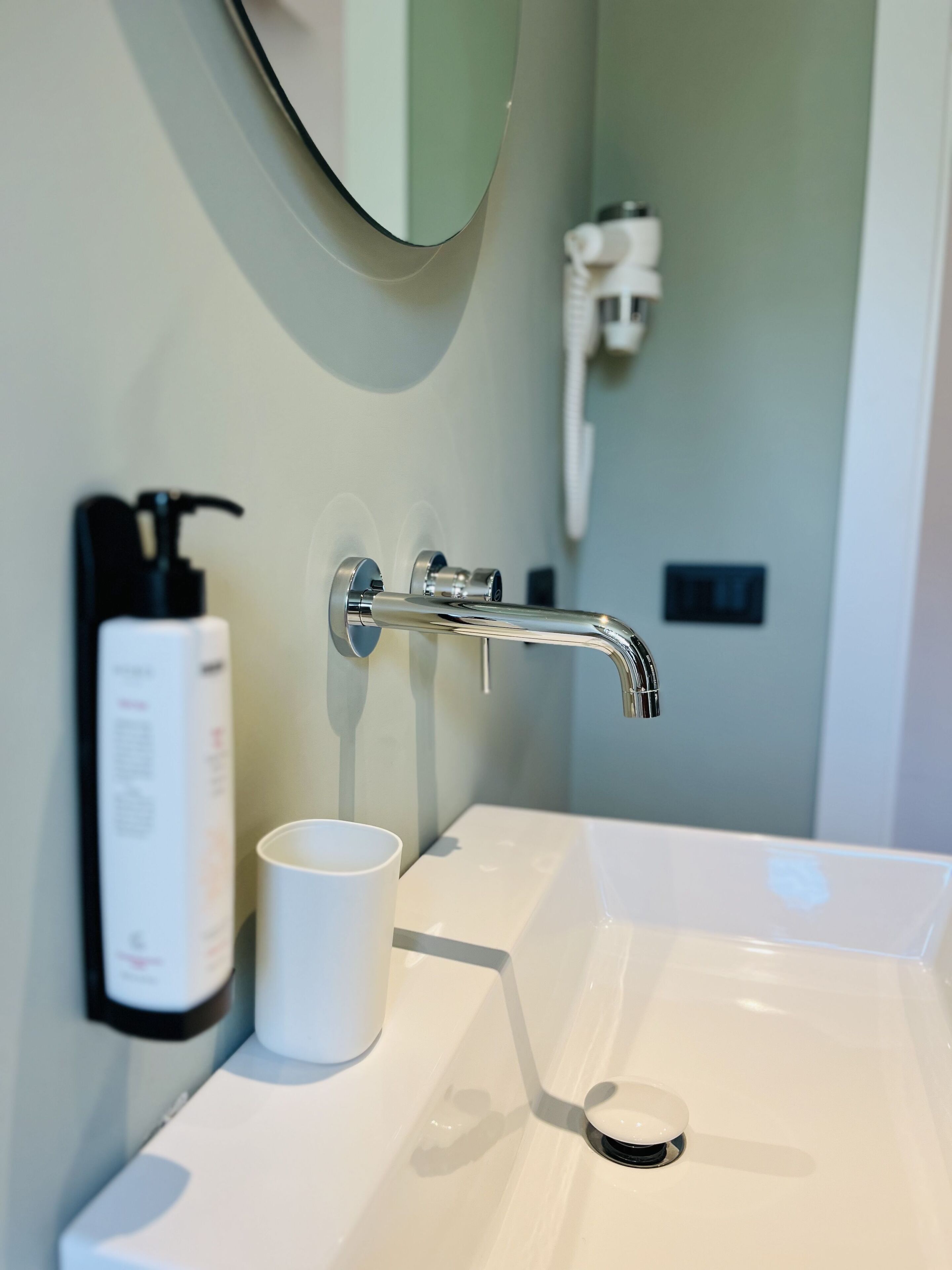 A bathroom with a white sink, a mirror, a faucet, and a bottle of hand soap.