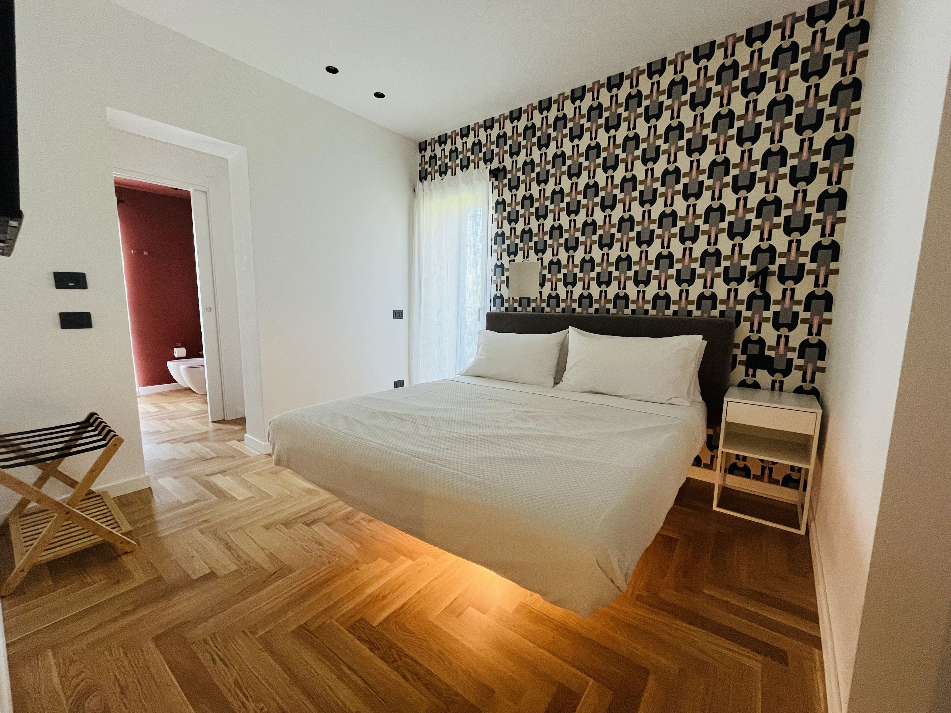 A modern bedroom with a large bed, wooden flooring, and a patterned wall.