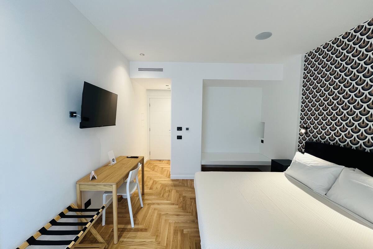 A modern hotel room with a bed, a desk, and a television.