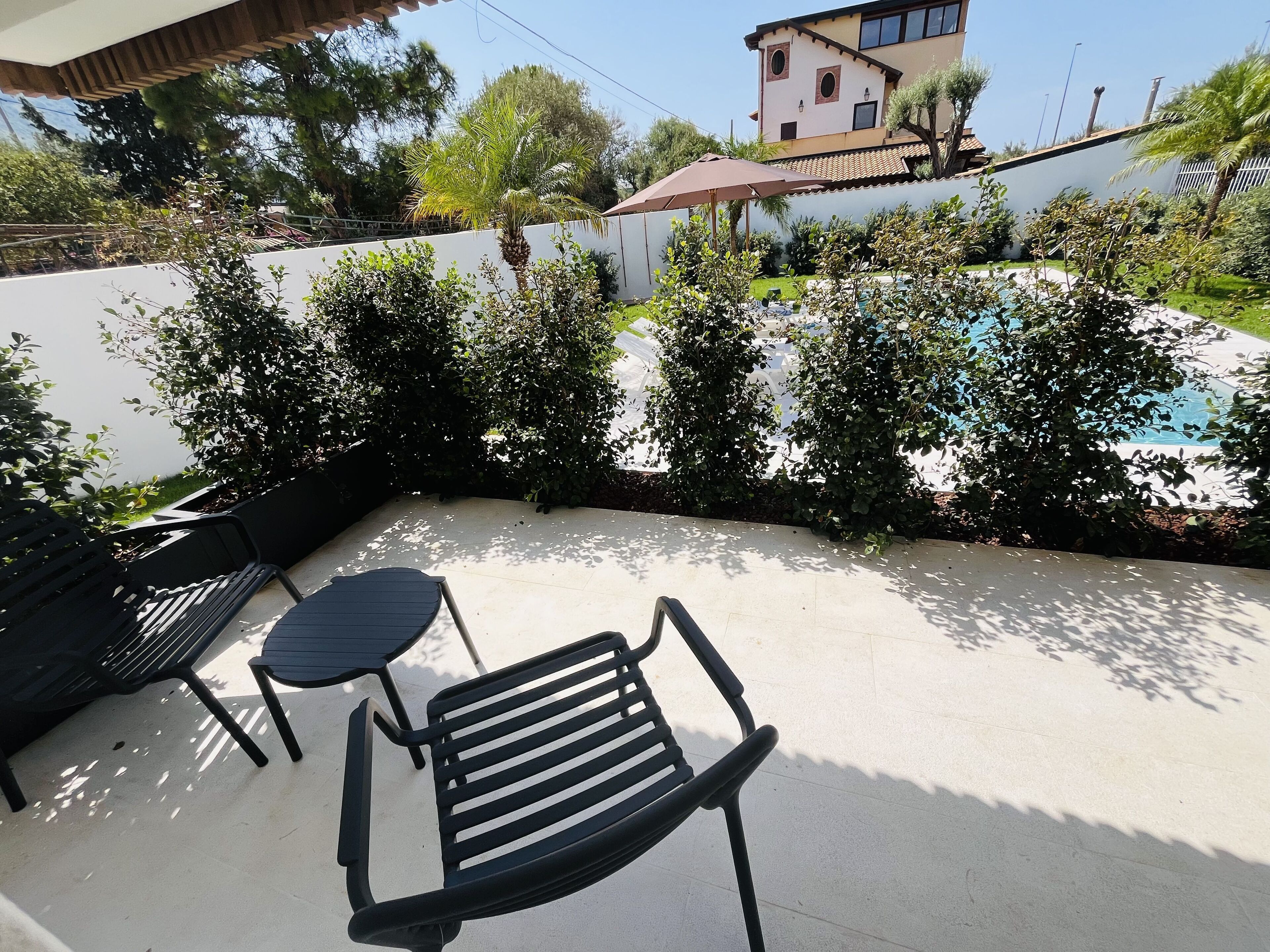 Área de pátio com piscina, móveis de exterior e parede branca com vegetação.